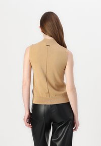 Beżowy, bezrękawnik dzianinowy z wysokim dekoltem, bezszwowymi ramionami i szwem na środku pleców. Teksturowana tkanina, dopasowany krój.