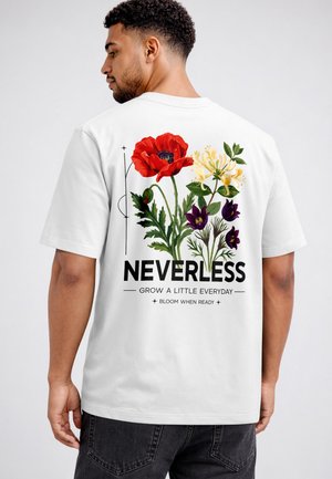 Mann trägt weißes T-Shirt mit farbenfroher Blumenillustration und Text „NEVERLESS Wachse jeden Tag ein wenig Blühe, wenn du bereit bist“ auf dem Rücken.