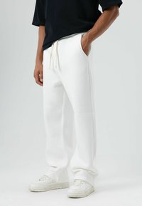 Witte joggingbroek met zijzakken, trekkoord in de taille en een ontspannen pasvorm. Gecombineerd met witte sneakers. Zachte stof en gladde textuur.