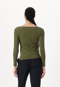 Långärmad, olivgrön topp med vid halsringning, figurnära design och slät textur. Tyget är stretchigt, vilket ökar komforten.