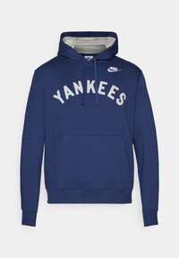 Jūras spēku sudraba krāsas kapuci krekls ar izšūtu "YANKEES" baltā krāsā. Iekļauts priekšējais kabata un Nike logo uz krūtīm. Kokvilnas maisījuma audums.