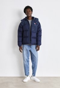 Giacca imbottita navy con zip frontale, dettagli in corduroy e taschino sul petto. Abbinata a jeans azzurri e sneakers bianche.