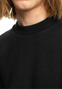 Felpa nera in cotone con collo alto, trama liscia e colletto a coste. Vista ravvicinata del tessuto e dei dettagli del collo.