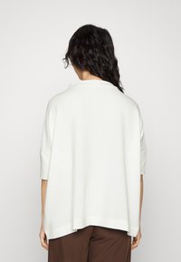 Biała, oversize'owa bluzka z krótkimi rękawami, o fakturze prążkowanej i lekko zaokrąglonym brzegu. Posiada subtelny kołnierz i luźny krój.