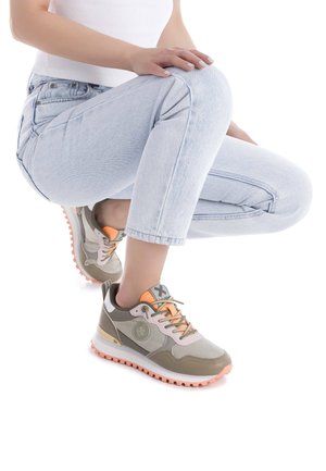 Zapatillas deportivas gris y beige con acentos naranjas, que cuentan con una suela texturizada, punta redonda y logo. Combinadas con jeans de color azul claro.