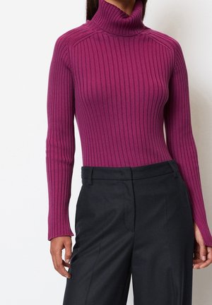 Femme portant un pull col roulé violet ajusté en maille côtelée à manches longues, associé à un pantalon noir taille haute et tailleur.