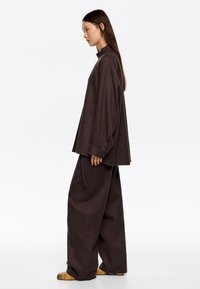 Conjunto suelto de color marrón que incluye una blusa de cuello alto y pantalones de pierna ancha. Tejido texturizado con una silueta relajada. Acentuado con zapatos de estampado.