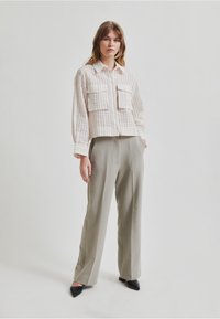 Camisa corta y texturizada en beige con dos bolsillos en el pecho. Combinada con pantalones gris de talle alto y ajustados, y zapatos negros de punta.