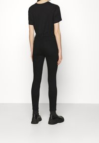 Camiseta negra y vaqueros pitillo en denim negro, diseño ajustado, textura lisa, combinados con botines negros. Detalle visible de costura trasera.