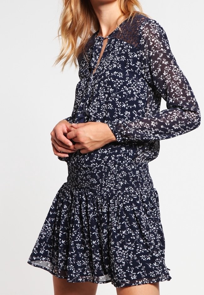Robe fleurie bleu marine avec de longues manches transparentes, taille smockée et jupe évasée. Motif de délicates fleurs blanches sur l'ensemble.