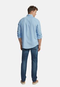 Himmelblauses Langarmhemd mit lockerer Passform und Rückenfalten-Detail, kombiniert mit blauen Jeans und beigen Schuhen. Einfaches, lässiges Design.