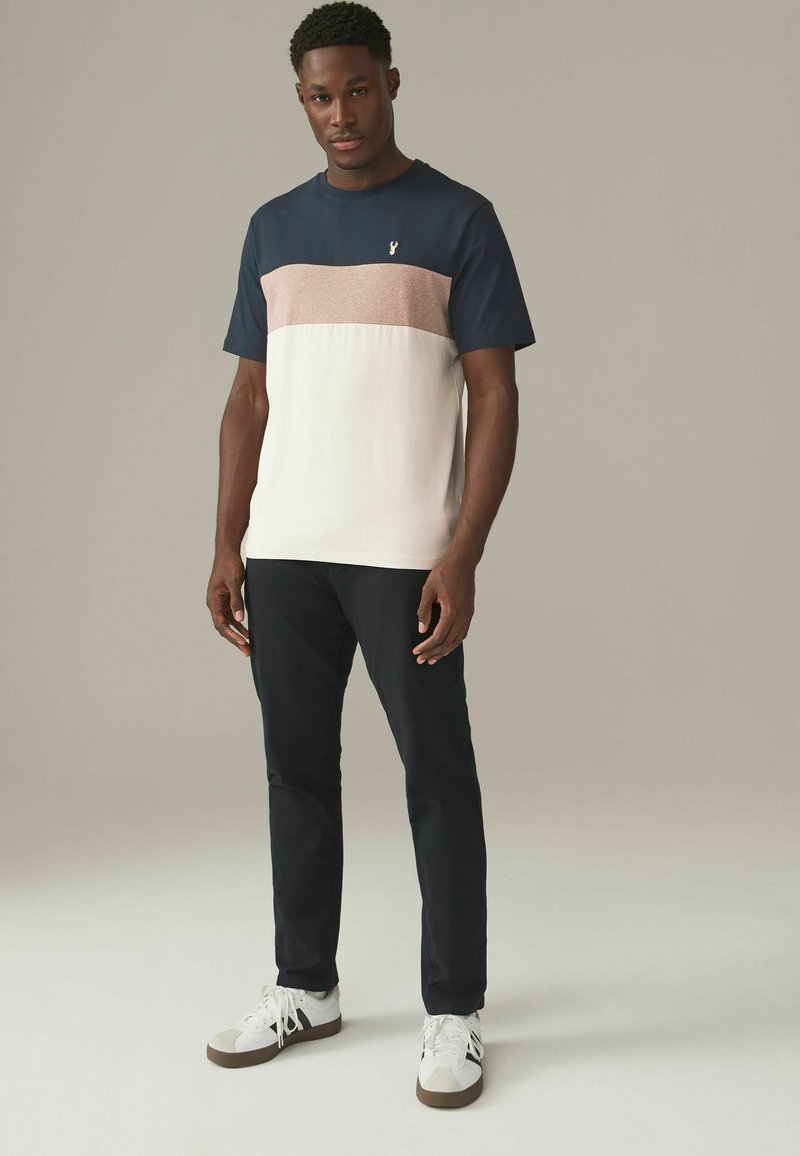 Herre farveblokket t-shirt har en marineblå top, en pink vandret stribe og en hvid bund. Lavet af en bomuldsblanding, med korte ærmer og rund hals.