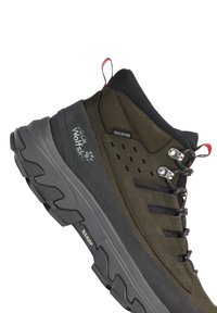 Outdoor-Wanderschuh in dunklem Olivgrün und Schwarz mit dicker, robuster Sohle, Metallösen und Zuglaschen, gebrandmarkt mit Jack Wolfskin- und Texapore-Logos.