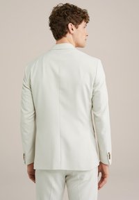 Helle Anzugjacke, taillierte Passform, glatte Textur, mit einem einzelnen Rückenschlitz und dezenten Knopfakzenten an den Ärmeln.