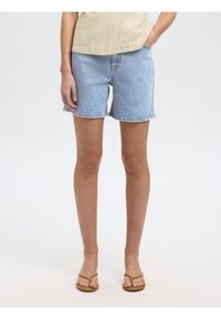 Shorts en denim de couleur bleu clair avec ourlet effiloché et poches latérales, associés à un haut à rayures beige et des tongs brunes. Design simple.
