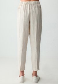 Pantaloni in lino beige chiaro con una cintura elastica, forma affusolata e orli risvoltati; tasca posteriore singola visibile.