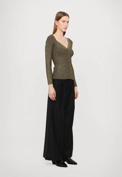 Langarm, diepe V-hals cardigan in metallic olijfgroen, met een slank silhouet en knoopsluiting, gedragen met ruime zwarte broeken.