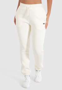 Joggers de color crema confeccionados en tejido suave, con cintura elástica y cordón ajustable, y puños ajustados. Detalle del logo pequeño en el bolsillo delantero.