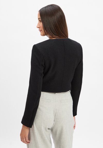 Pull cropped noir avec de longues manches côtelées. Le tissu semble doux avec une texture lisse. La partie arrière présente un simple détail de couture.