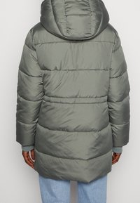 Chaqueta acolchada de color verde apagado, con capucha, costuras horizontales y puños acanalados. Tejido suave y brillante con un diseño voluminoso.