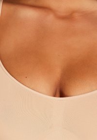 Huidkleurige tanktop met een ruime halslijn en geribbelde textuur, uitlopend naar een aansluitende silhouet, met minimalistische ontwerpelementen.