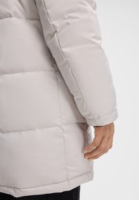 Cappotto imbottito di un grigio chiaro con una trama liscia simile al nylon. Presenta una linea dritta e tasche laterali nascoste.