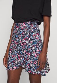 Blommig omlottskjol i mörk marinblått med rosa och blå blommor, i ett lätt material och med utsvängd nederkant. Knytning i midjan med volangkanter.