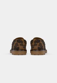 Mocassins com padrão de camuflagem castanho e preto, com solas de borracha grossas e castanhas claras, mostrados de trás sobre um fundo branco.