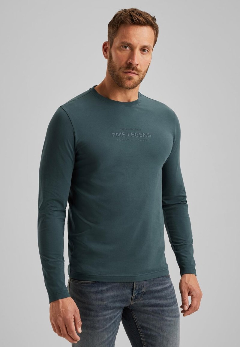 Langarmshirt in teal met ronde hals, met "PME LEGEND" in reliëf op de borst, gecombineerd met blauwe spijkerbroek.