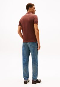 Camisa polo de manga corta marrón, jeans de mezclilla azul y zapatos de cuero oscuros; texturas suaves y diseño clásico con un corte relajado.