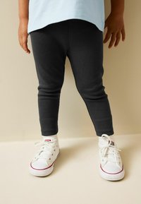 Tmavé rebrované legíny v kombinácii s bielymi plátenými teniskami s červenými akcentmi. Oblečenie dopĺňa svetlomodrá blúzka s voľným strihom.