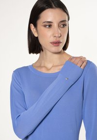 Blauwe trui met lange mouwen en een ronde halslijn, ribbelstructuur en knoopaccent bij de mouw. Lichtgewicht en aansluitend ontwerp.
