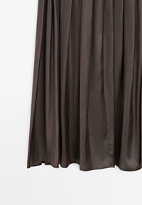 Mörkbrunt silkesliknande tyg som hänger vertikalt med mjuka veck och en slät, glänsande yta, mot en enkel vit bakgrund.