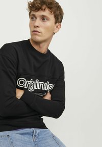 Sudadera negra con cuello redondo, mangas con puños y un logo gráfico blanco en el pecho. Material de algodón con una textura lisa.