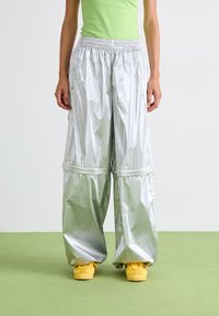 Pantalons larges argentés et brillants avec une taille élastique froncée ; associés à des baskets jaunes. Le tissu semble léger et texturé.