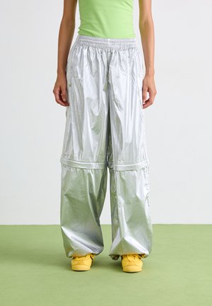 Zilveren, glanzende wijde broek met een elastische tailleband; gecombineerd met gele sneakers. De stof lijkt lichtgewicht en gestructureerd.