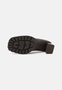 Chaussure à talon marron avec une semelle extérieure en caoutchouc texturée présentant un motif en losange et un talon bloc solide pour la stabilité.