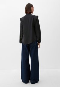 Zwart longsleeve shirt met gestructureerde schouderaccenten, gecombineerd met high-waisted blauwe denim jeans met een rauwe zoom.