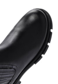 Zwarte leren enkelboot met een ronde neus, gestructureerde zijkanten en een robuuste zool met kenmerkende profielpatronen.