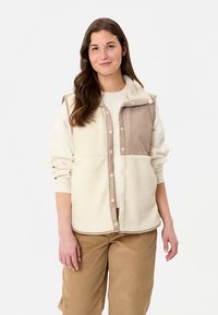 Fleece vest in cream and beige with snap buttons, featuring a high collar and a soft texture. Worn over a light sweater, layered look.