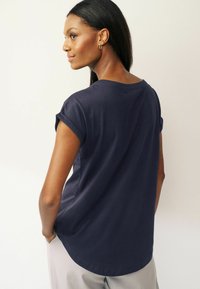 Marinblå t-shirt med kort ärm och avslappnad passform, med rundad nederkant, tillverkad av mjuk bomull. Har uppvikta ärmslut och en enkel design.