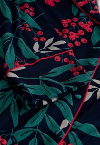Námořnická tkanina s vzorem zelených listů a červených bobulí, s kontrastním růžovým lemem. Měkká textura s hladkým splývavým designem.