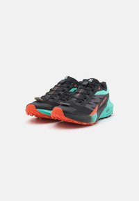 Scarpe da trail running nere con tomaia in mesh, dettagli turchesi e suola arancione brillante. Presentano un sistema di lacci rapidi e una suola robusta.