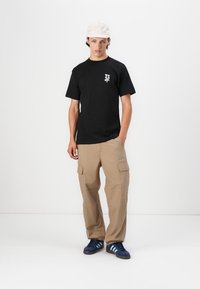 Sort bomulds T-shirt med et lille logo print, parret med løstsiddende beige cargo bukser med sidelommer og blå sneakers.