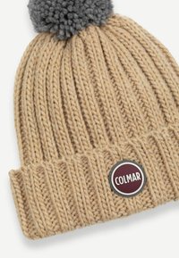 Berretto lavorato a maglia beige con costine testurizzate. Presenta un pom-pom grigio sulla parte superiore e un'etichetta circolare bordeaux con il testo "COLMAR".