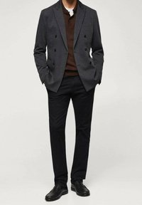 Blazer grigio doppiopetto, polo marrone sotto, pantaloni neri e mocassini neri. Tessuto morbido con una vestibilità su misura e dettagli sottili.