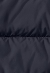 Marine pufferjack met een gladde textuur en een subtiele glans; geborduurd ontwerp met horizontale naden voor isolatie.