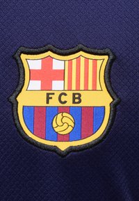 Έμβλημα ποδοσφαιρικής ομάδας FC Barcelona με κόκκινο σταυρό, κίτρινες και κόκκινες ρίγες, μπλε και κόκκινες κάθετες ρίγες και κίτρινη ποδοσφαιρική μπάλα σε μπλε ύφασμα.
