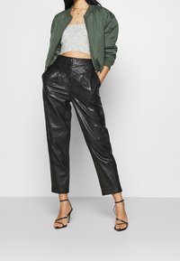 Zielona pikowana kurtka bomberka, szary krótki top, czarne spodnie ze skóry o wysokim stanie z plisami oraz czarne sandały na wysokim obcasie z paskami.