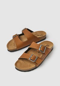Sandales en cuir marron avec deux sangles réglables et boucles métalliques argentées, offrant une semelle en liège et une semelle en caoutchouc texturé.